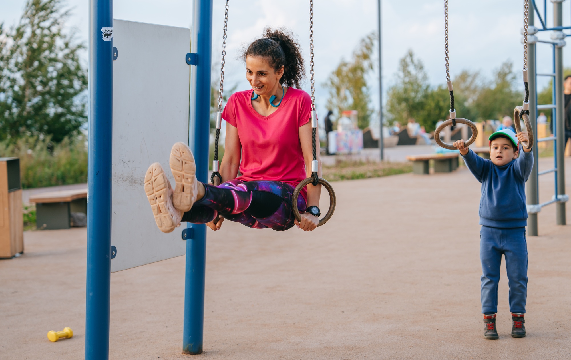 strong girl athlete is an easy athlete who trains on rings on the playground with son in the summer.